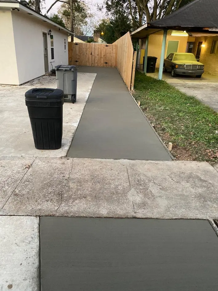 Completed concrete walkway beside a house and wooden fence